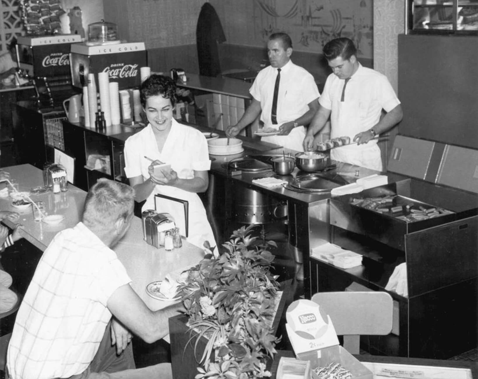 Historical black and white photo of workers inside of a skyline chili restaurant serving people at the counter