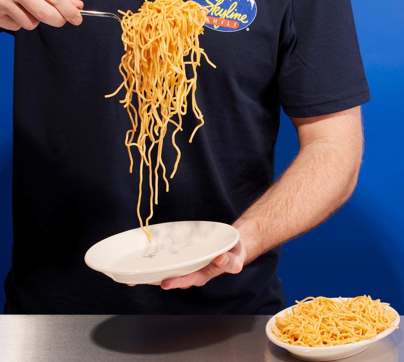 Man holding empty plate in one hand with a spoonful of noodles in the other hand
