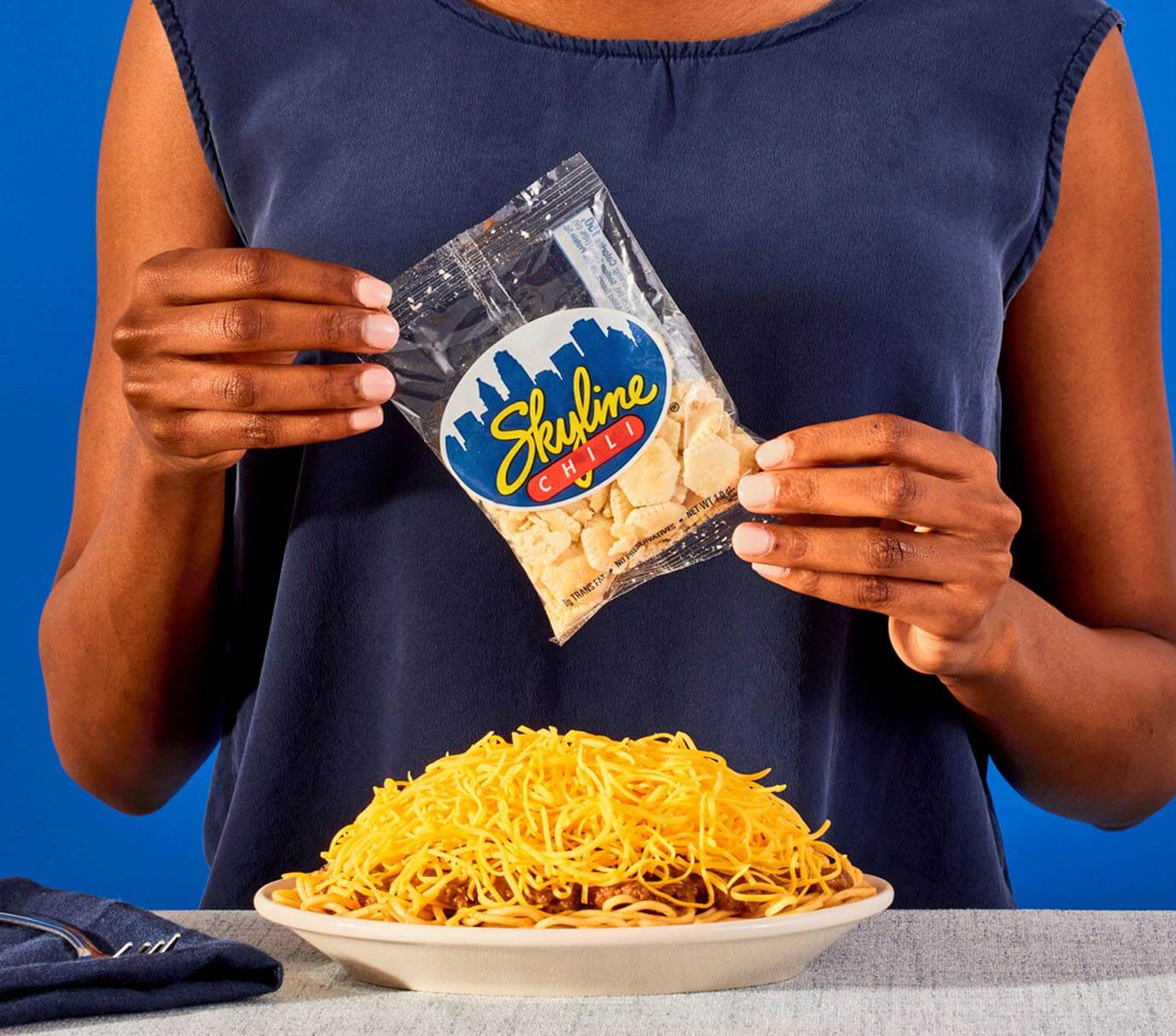 Woman holding back of Skyline oyster crackers. On table in front of her sits a skyline way.