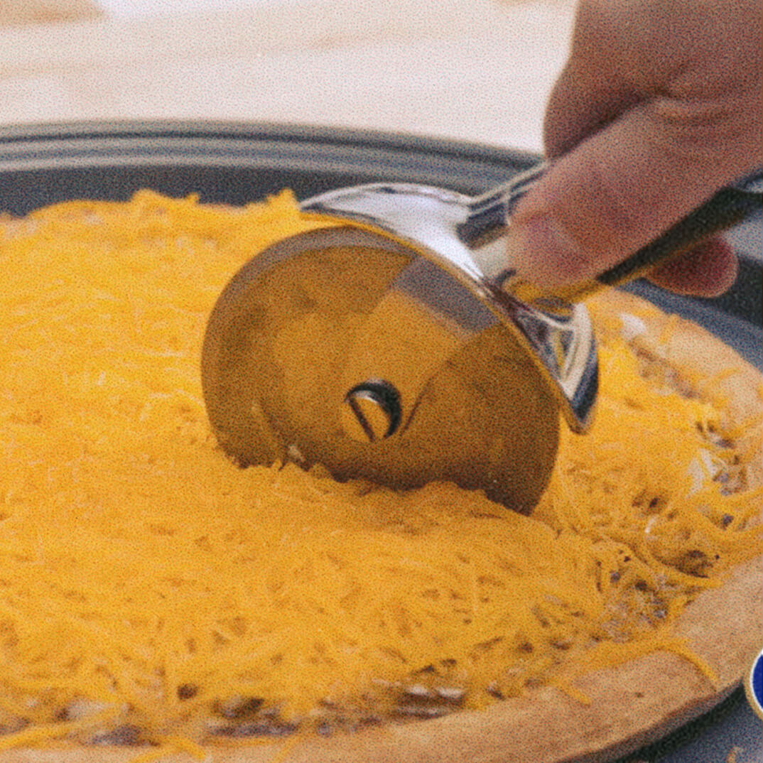 pizza cutter being used to cut a skyline pizza