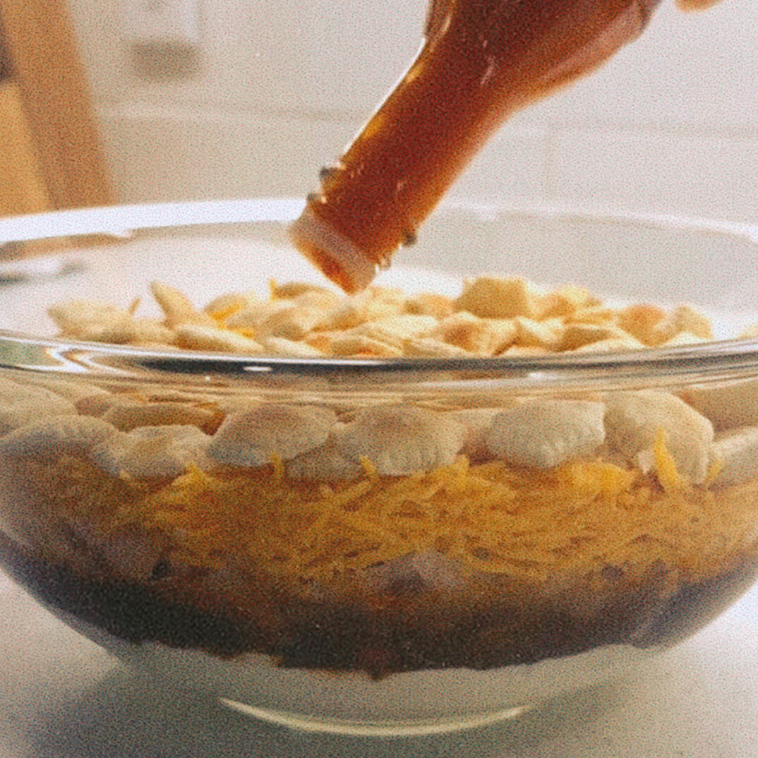 Bowl with layered ingredients and hot sauce being poured on top