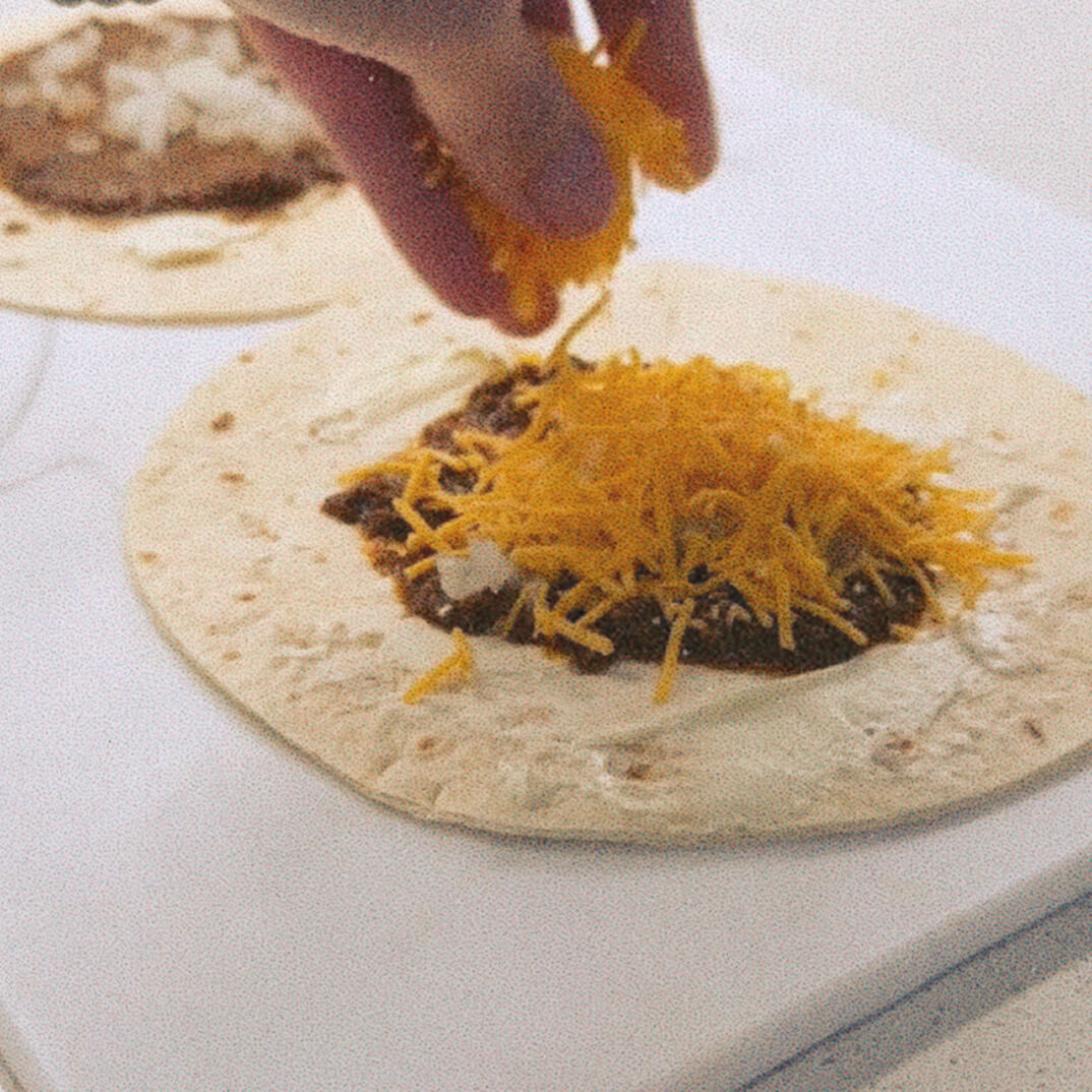 Tortilla with skyline chili in the center, and shredded cheese being sprinkled on top