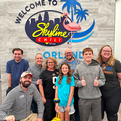 Family smiling in front of Welcome to Skyline Chili Orlando sign