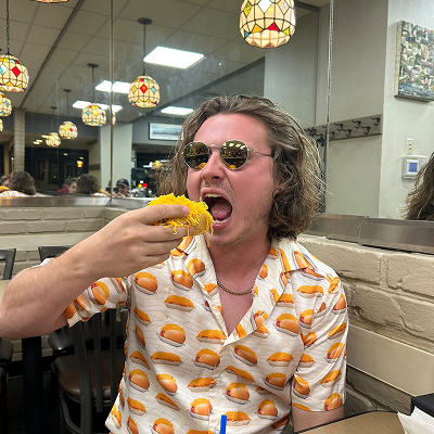 Guy wearing sunglasses and a skyline shirt eating coney